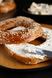 Photo of Delicious bagel with tofu cream cheese and knife on black wooden table, closeup