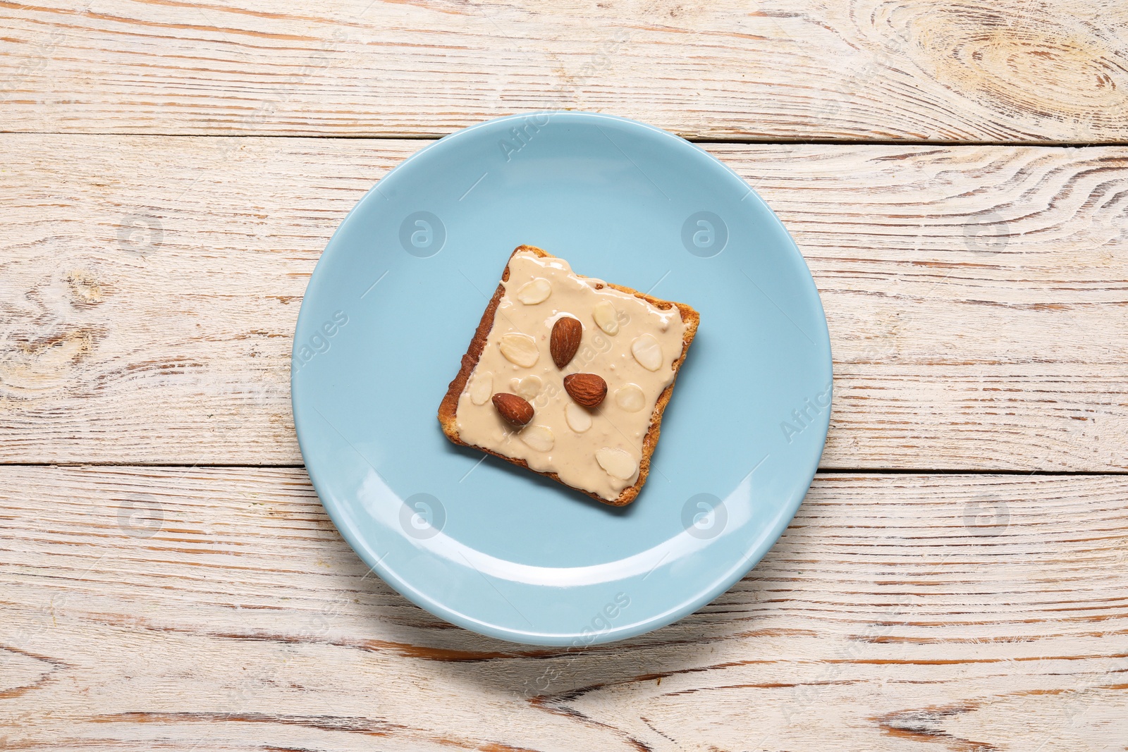 Photo of Toast with tasty nut butter and almonds on light wooden table, top view