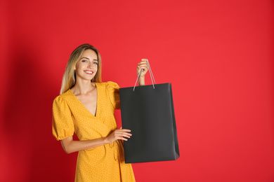 Photo of Happy young woman with shopping bag on red background. Black Friday Sale