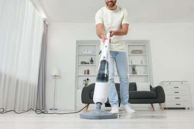 Happy man cleaning floor with steam mop at home, closeup. Low angle view