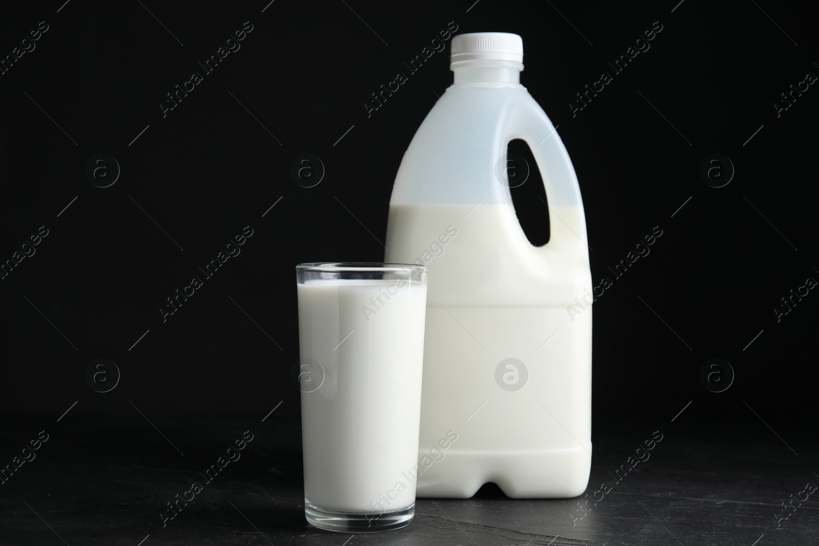 Photo of Gallon bottle and glass of milk on black table