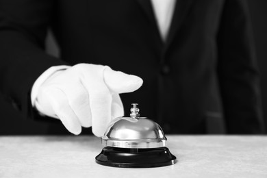Photo of Butler ringing service bell at table on black background, closeup