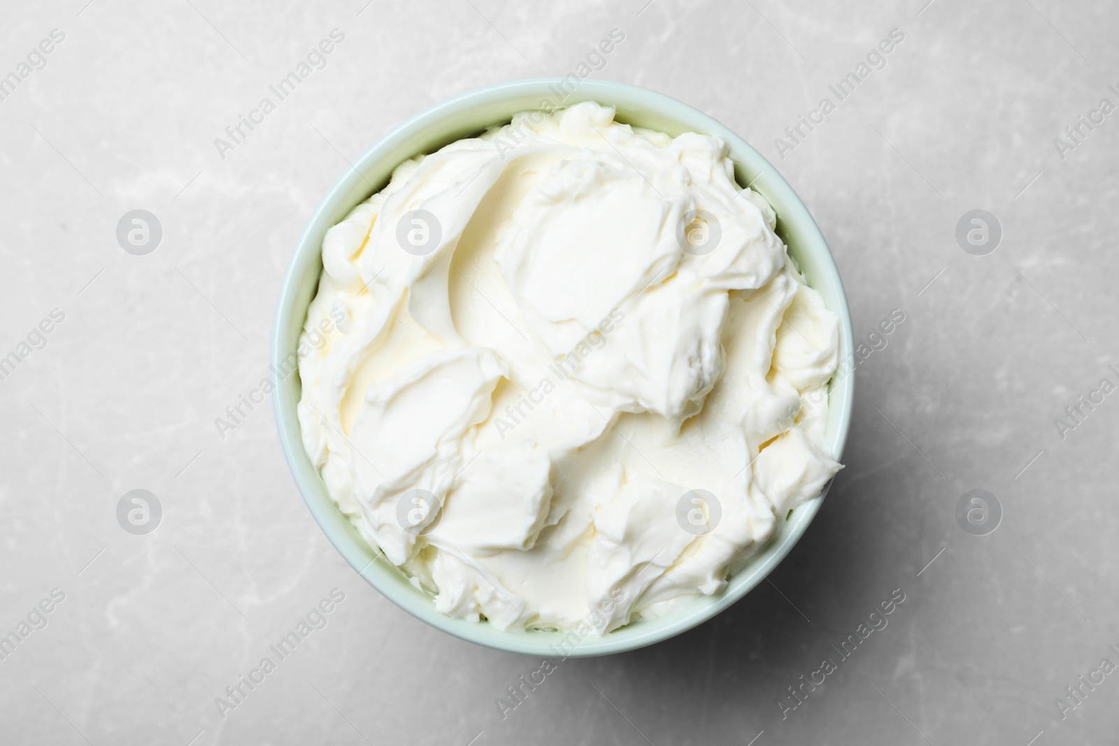 Photo of Bowl of tasty cream cheese on grey table, top view