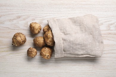 Photo of Sack with fresh Jerusalem artichokes on white wooden table, flat lay