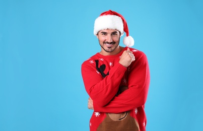 Photo of Portrait of young man in Christmas sweater and Santa hat on light blue background