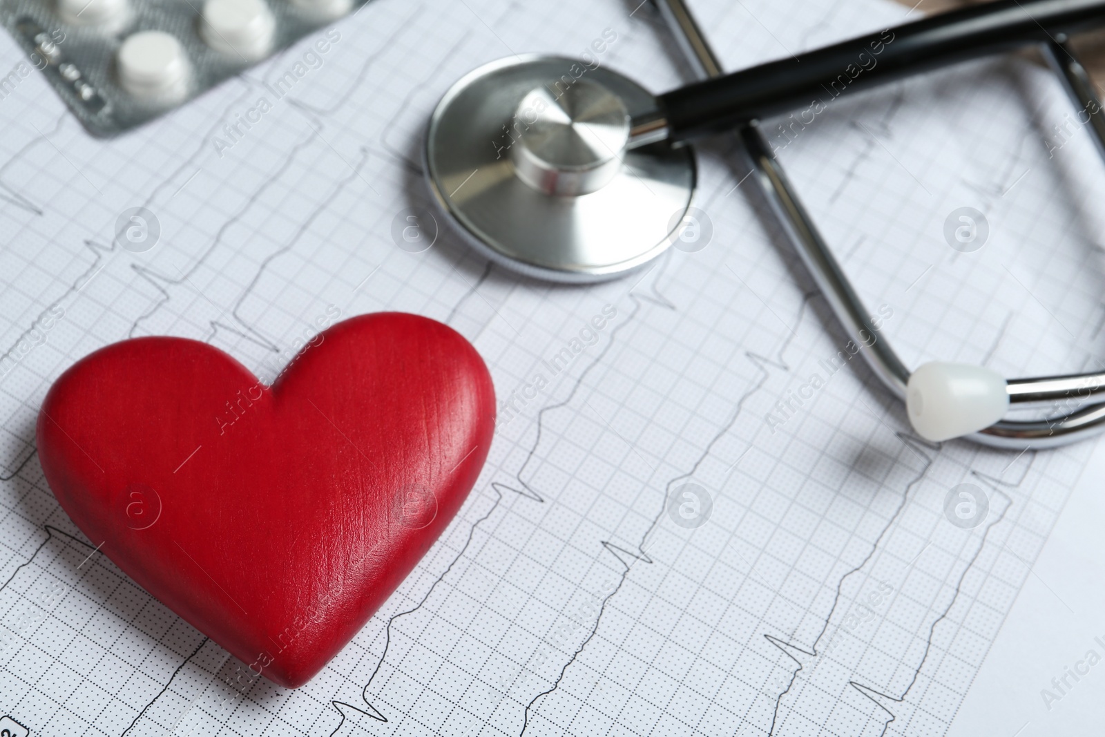 Photo of Red decorative heart, pills and stethoscope on cardiogram report, closeup