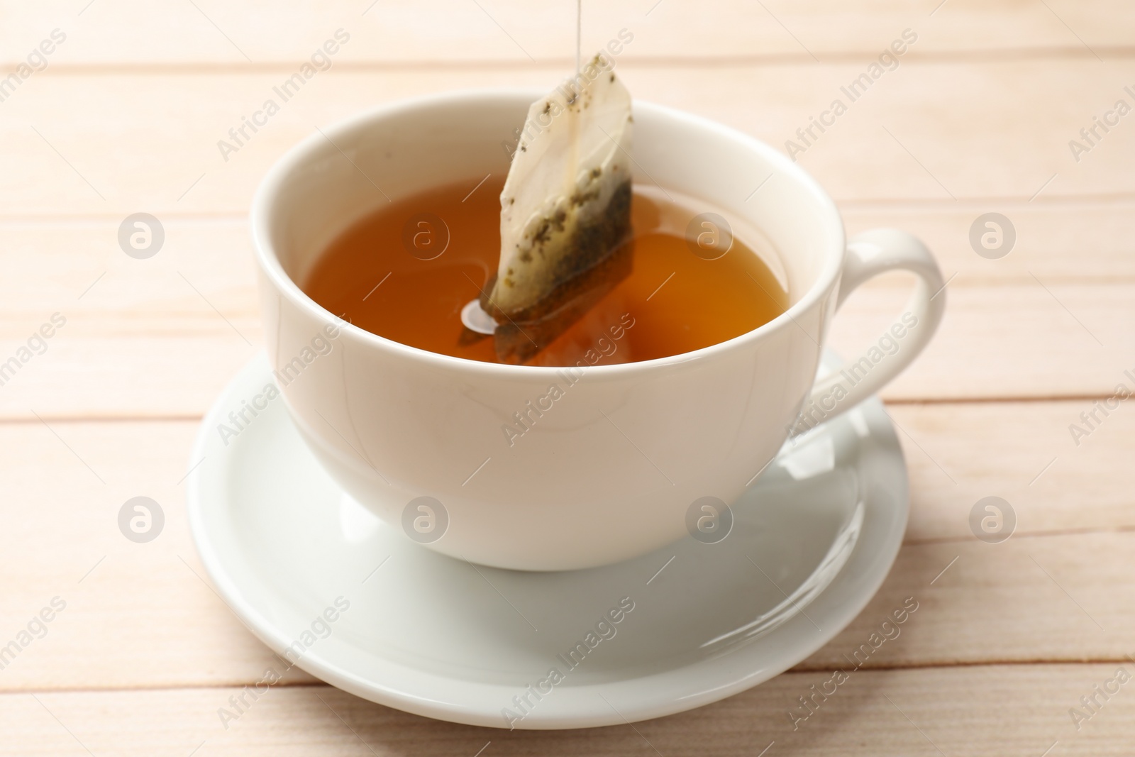 Photo of Putting tea bag in cup on light wooden table, closeup