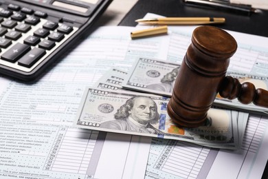 Photo of Tax return forms, dollar banknotes, gavel and calculator on table, closeup