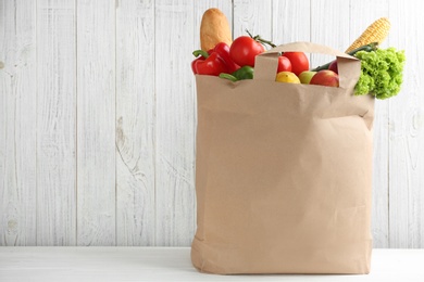 Photo of Shopping paper bag with different groceries on table against white wooden background. Space for text