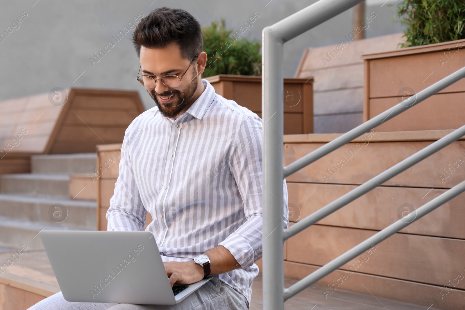 Photo of Handsome young man using laptop on bench outdoors