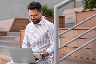 Photo of Handsome young man using laptop on bench outdoors