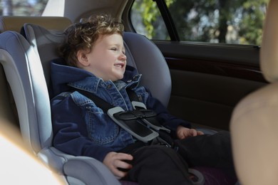 Cute little boy sitting in child safety seat inside car