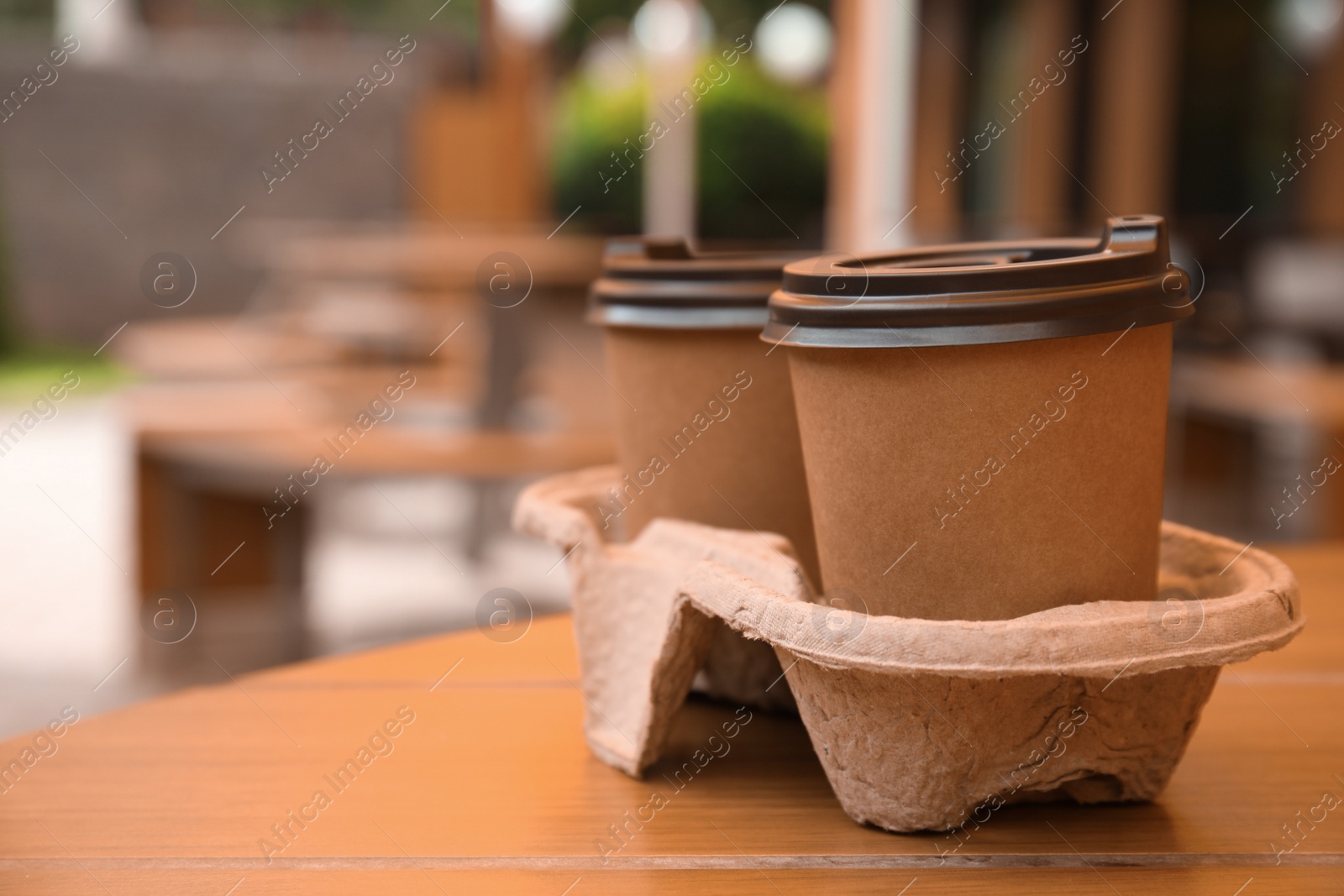 Photo of Takeaway paper coffee cups with plastic lids in cardboard holder on wooden table outdoors, space for text