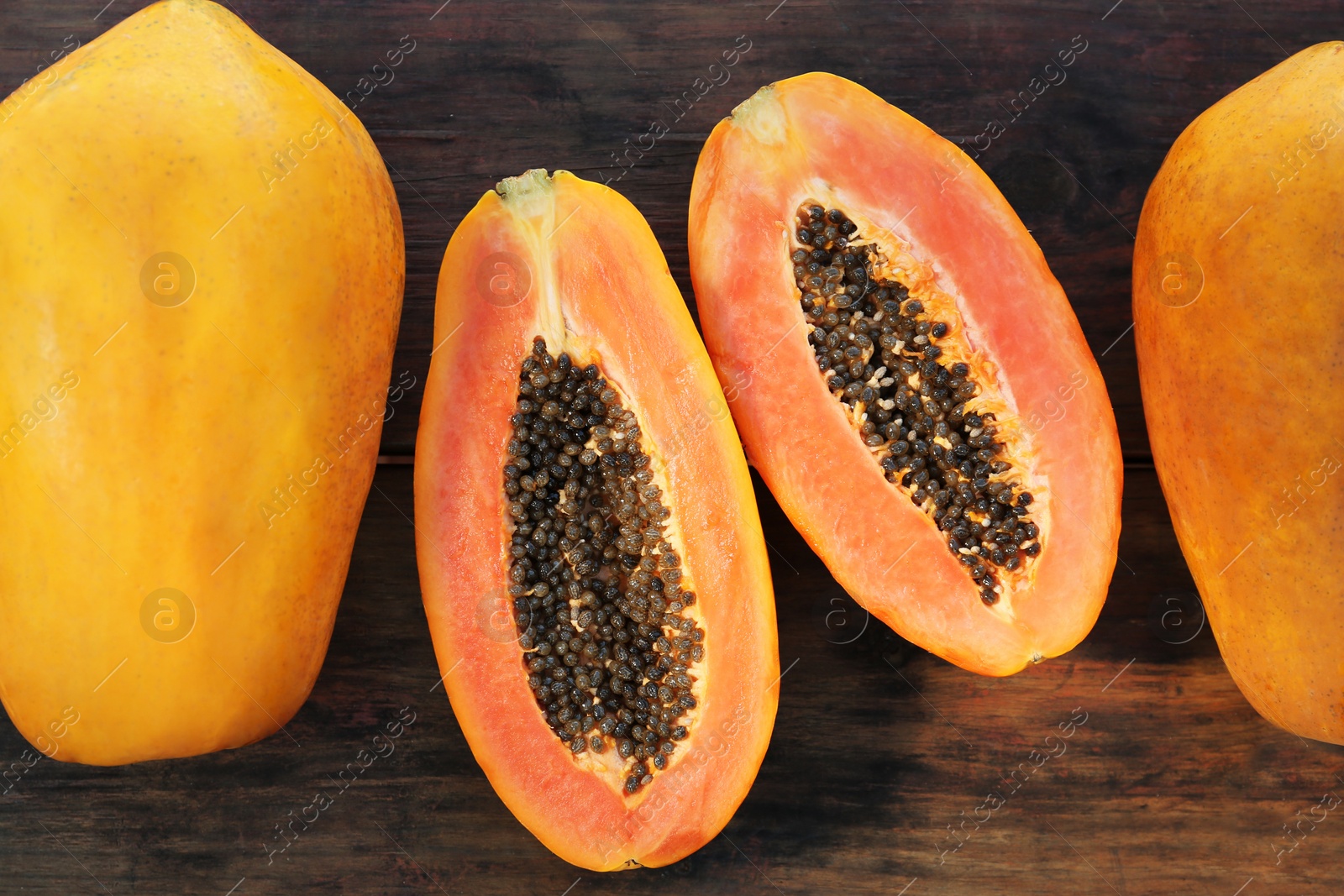 Photo of Fresh ripe cut and whole papaya fruits on wooden table, flat lay