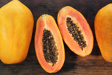 Photo of Fresh ripe cut and whole papaya fruits on wooden table, flat lay