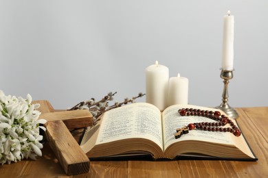 Photo of Church candles, cross, rosary beads, Bible, snowdrops and willow branches on wooden table against light background