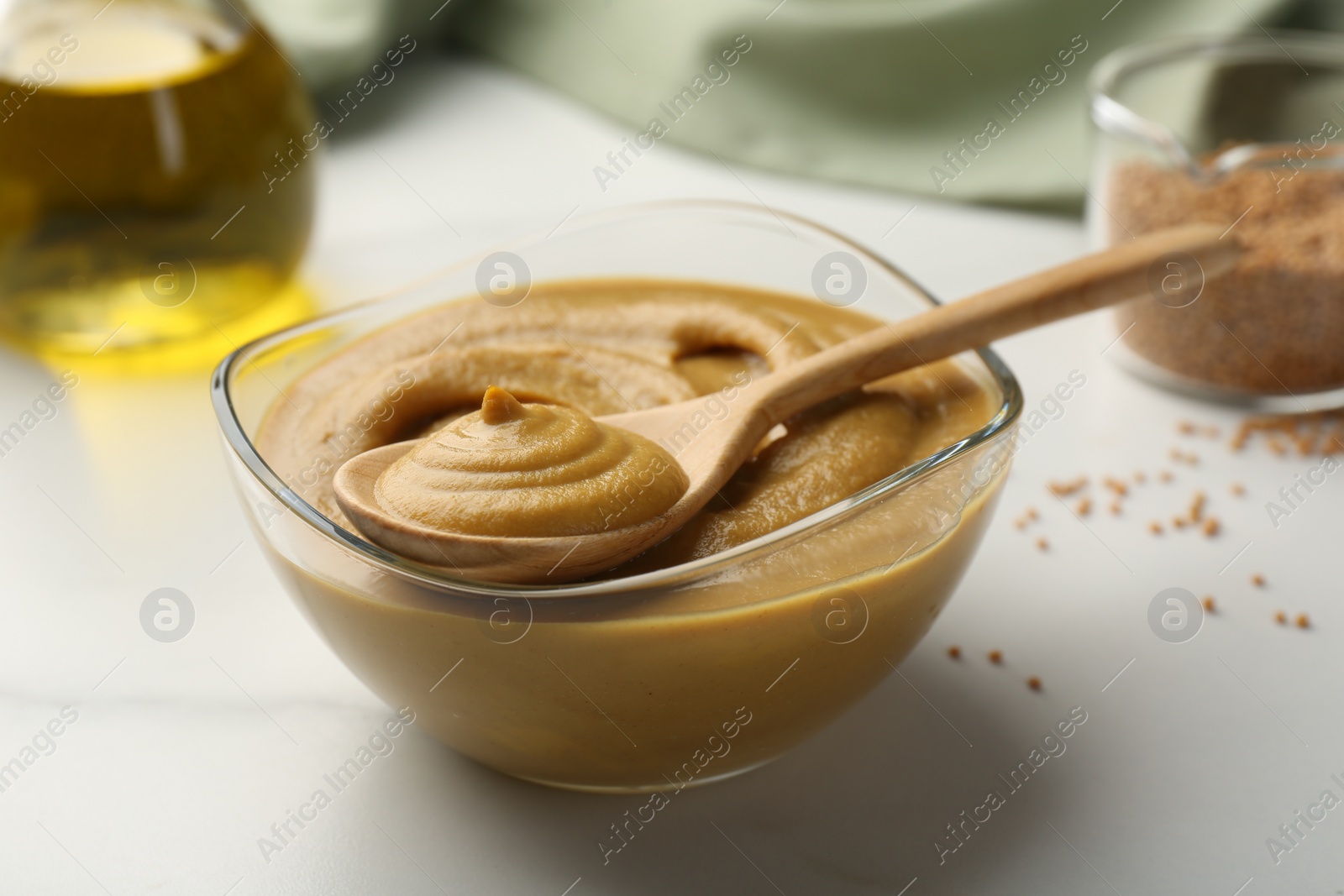 Photo of Spoon and glass bowl with tasty mustard sauce on white table, closeup