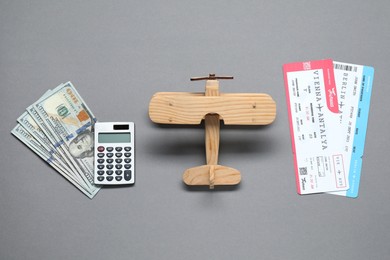 Photo of Flat lay composition with dollars, wooden model of plane and tickets on light grey table. Business trip