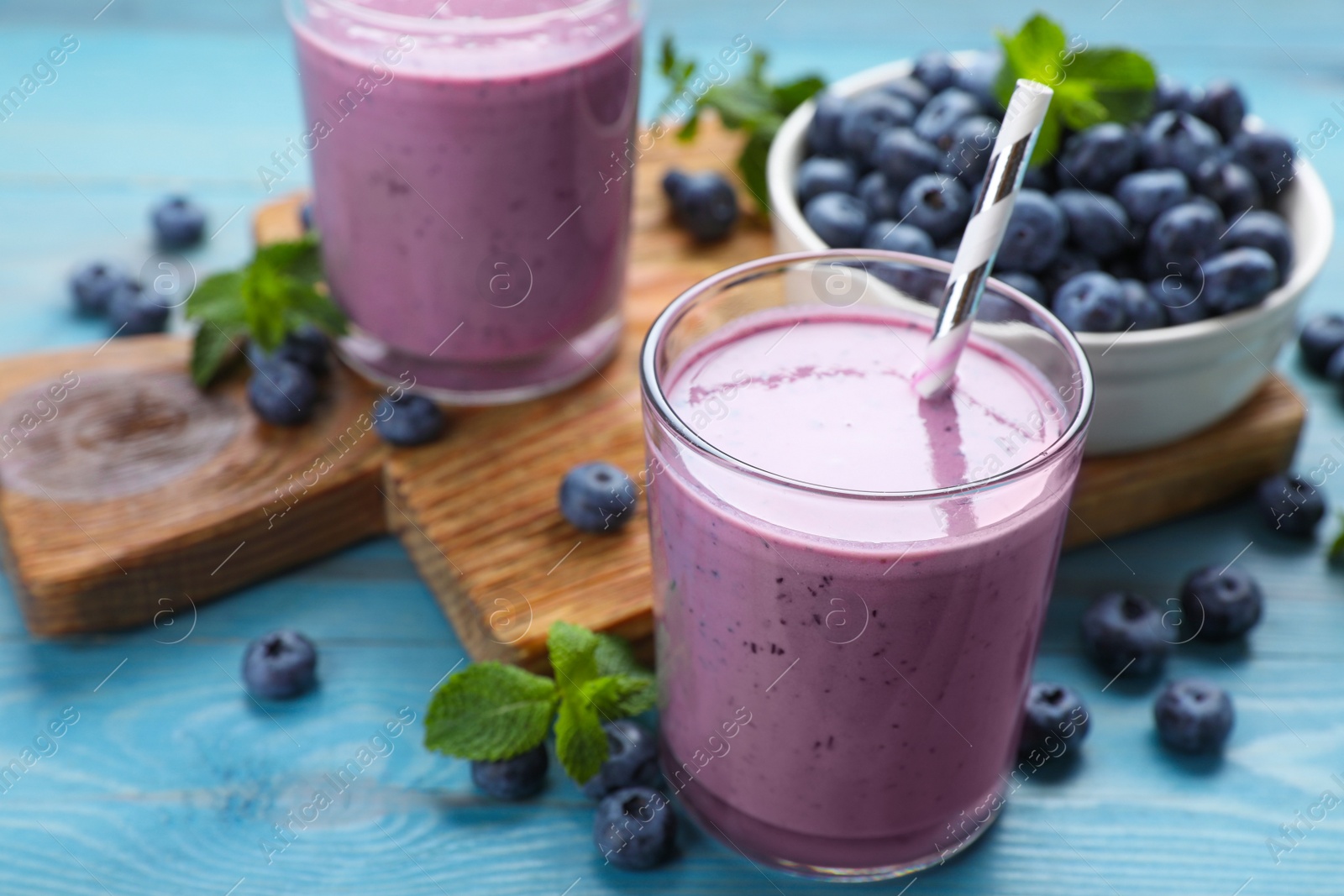 Photo of Glass of blueberry smoothie with mint and fresh berries on turquoise wooden table, closeup