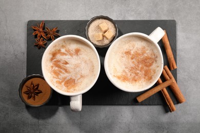 Photo of Cups of delicious eggnog with anise and cinnamon on grey table, flat lay