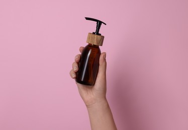 Woman holding bottle of cosmetic product on pink background, closeup