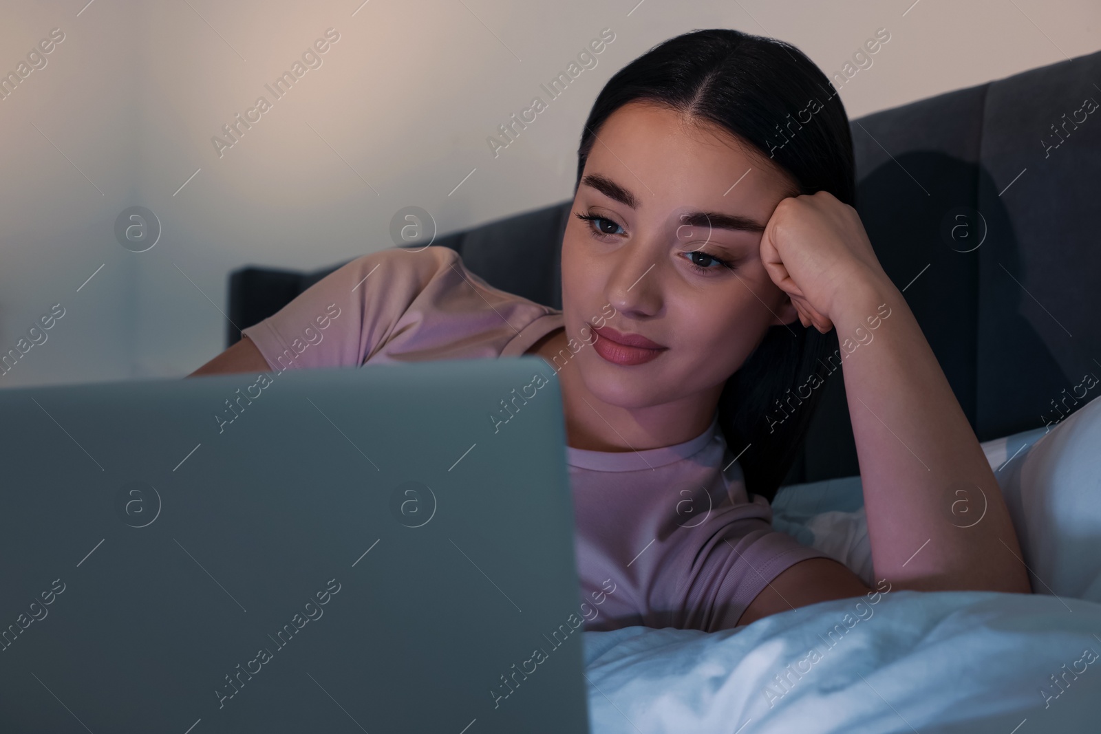 Photo of Young woman using laptop in bed at night. Internet addiction