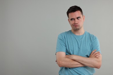 Photo of Resentful man with crossed arms on grey background, space for text