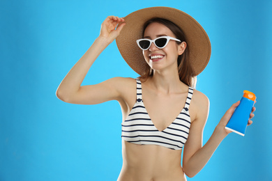 Young woman with sun protection cream on light blue background