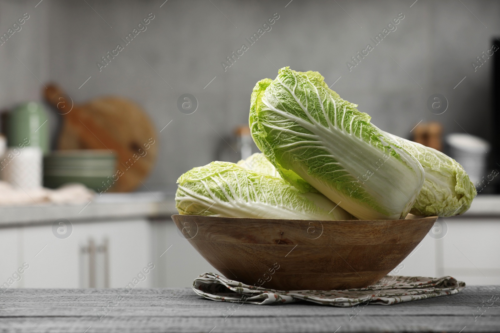 Photo of Fresh Chinese cabbages in bowl on grey wooden table indoors, space for text