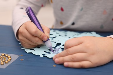 Photo of Little child making Christmas craft at blue wooden table, closeup