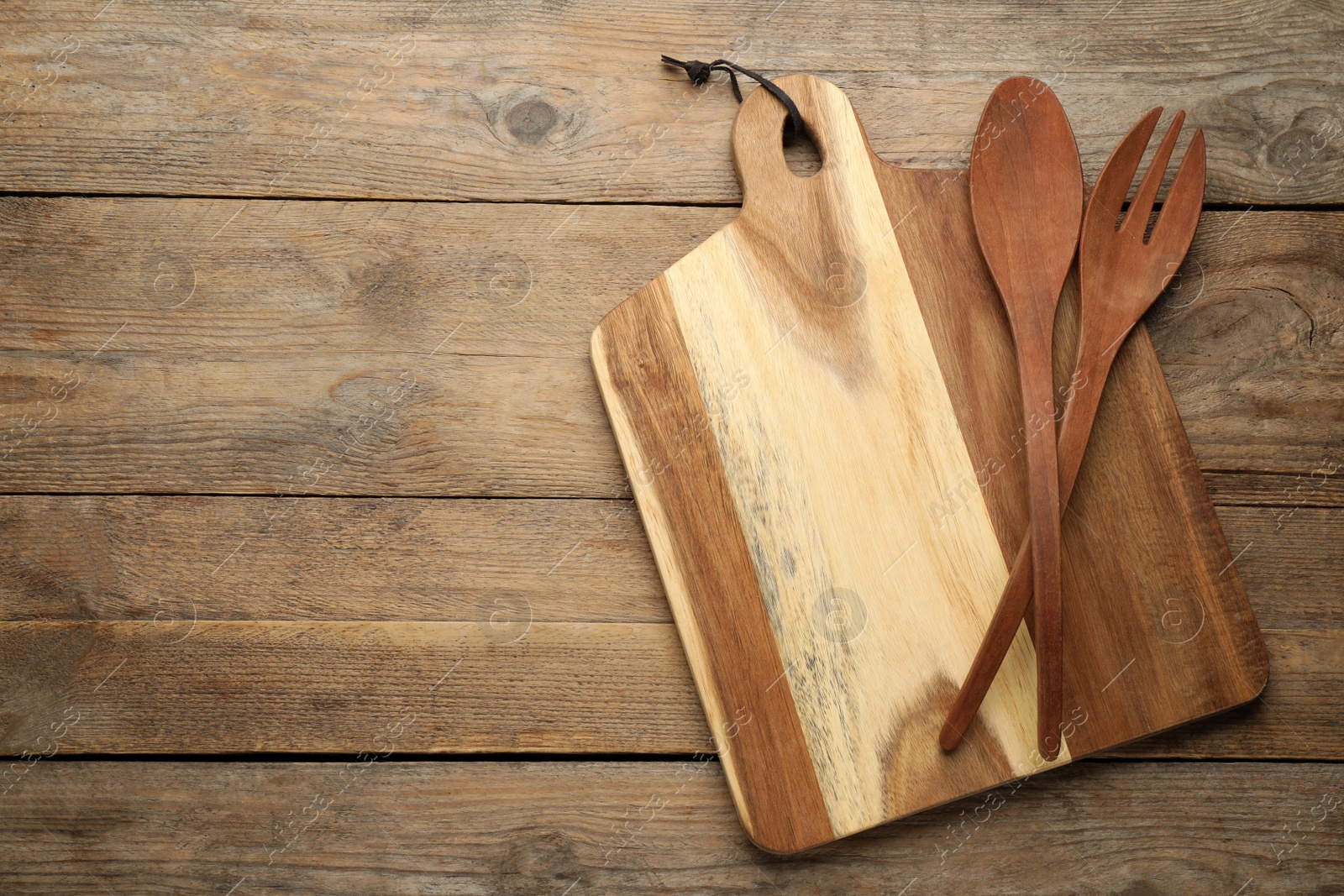 Photo of Cutting board, spoon and fork on wooden table, top view with space for text. Cooking utensils