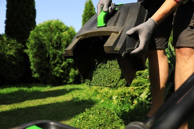 Photo of Man removing grass out of lawn mower box in garden, closeup