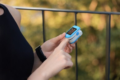 Woman checking pulse with blood pressure monitor on finger after training outdoors, closeup