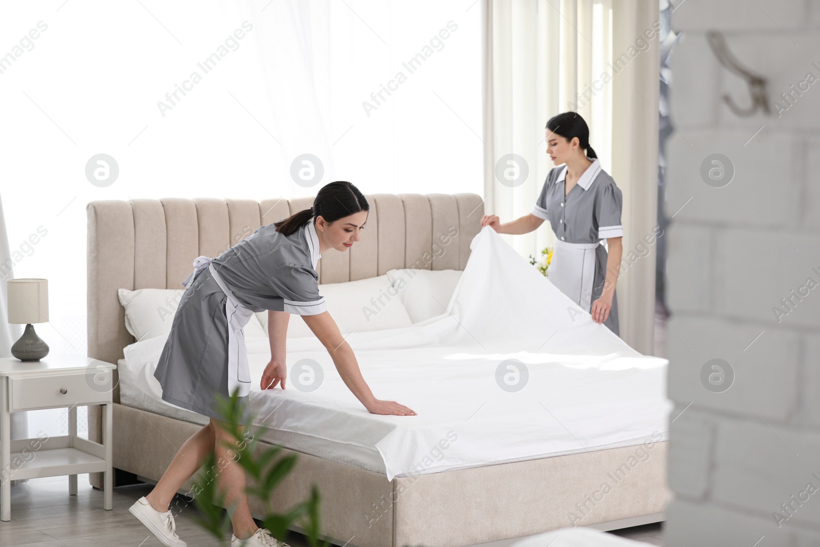 Photo of Young chambermaids making bed in hotel room