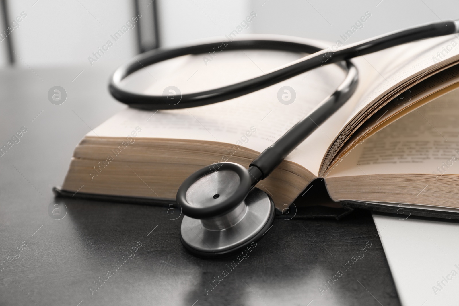 Photo of Open student textbook and stethoscope on grey table indoors, closeup. Medical education