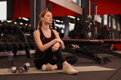 Photo of Athletic young woman with earphones on mat in gym