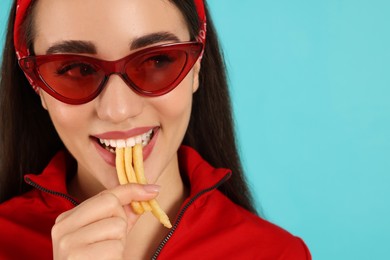 Beautiful young woman eating French fries on light blue background, closeup