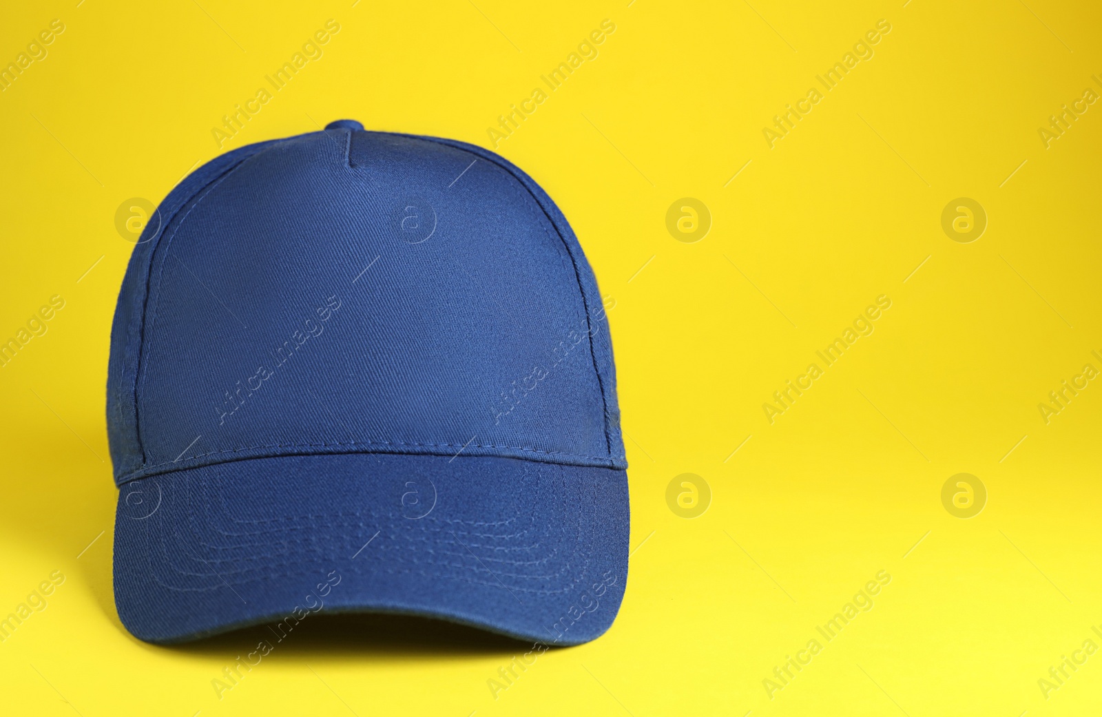 Photo of Stylish blue baseball cap on yellow background. Space for text