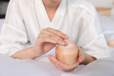 Photo of Woman taking hand cream from jar indoors, closeup