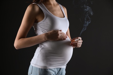 Photo of Pregnant woman smoking cigarette on black background, closeup