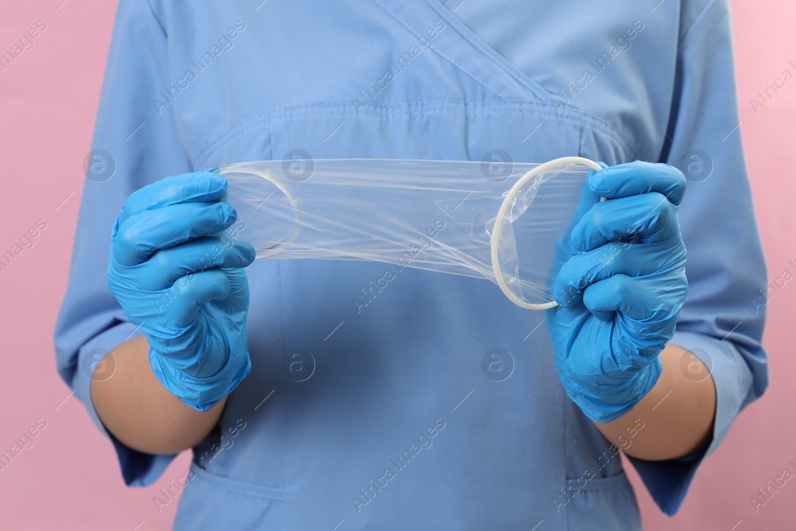 Photo of Doctor with unrolled female condom on pink background, closeup. Safe sex