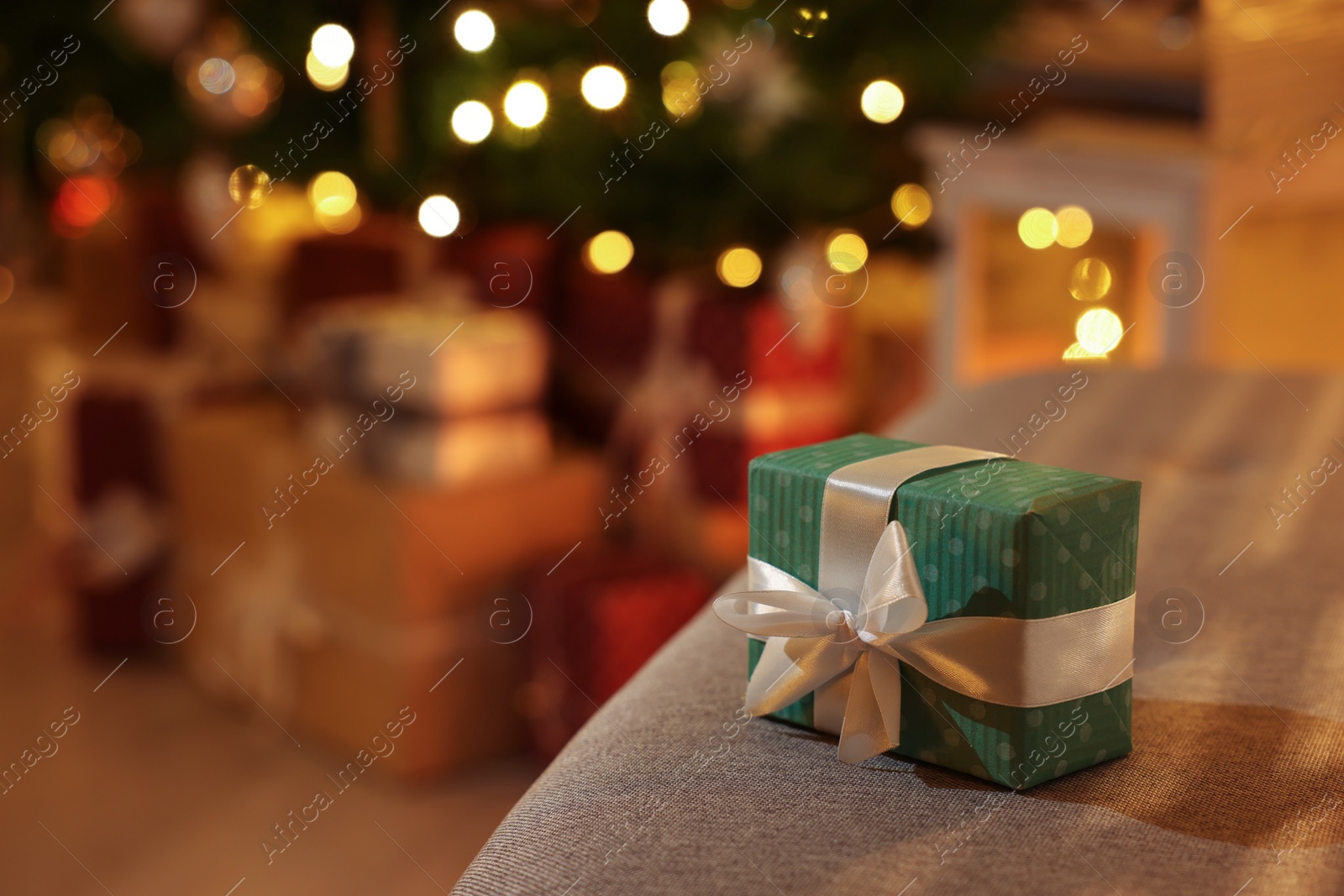 Photo of Christmas gift box on sofa against blurred lights indoors. Space for text