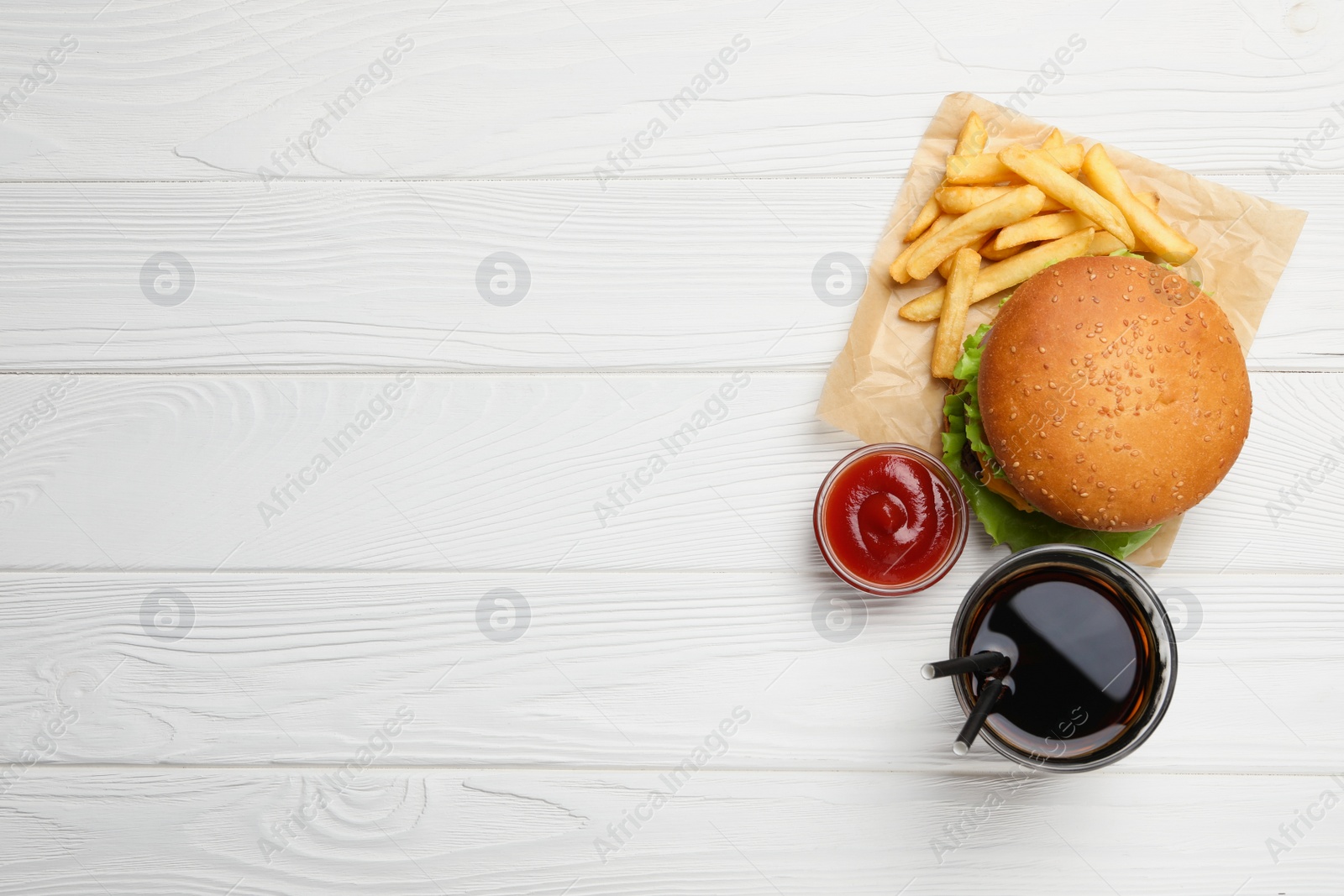 Photo of French fries, tasty burger, sauce and drink on white wooden table, flat lay. Space for text