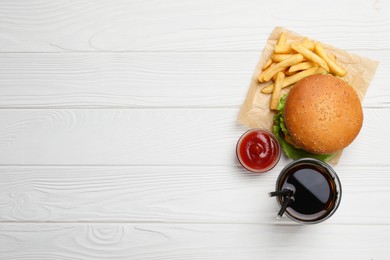 French fries, tasty burger, sauce and drink on white wooden table, flat lay. Space for text