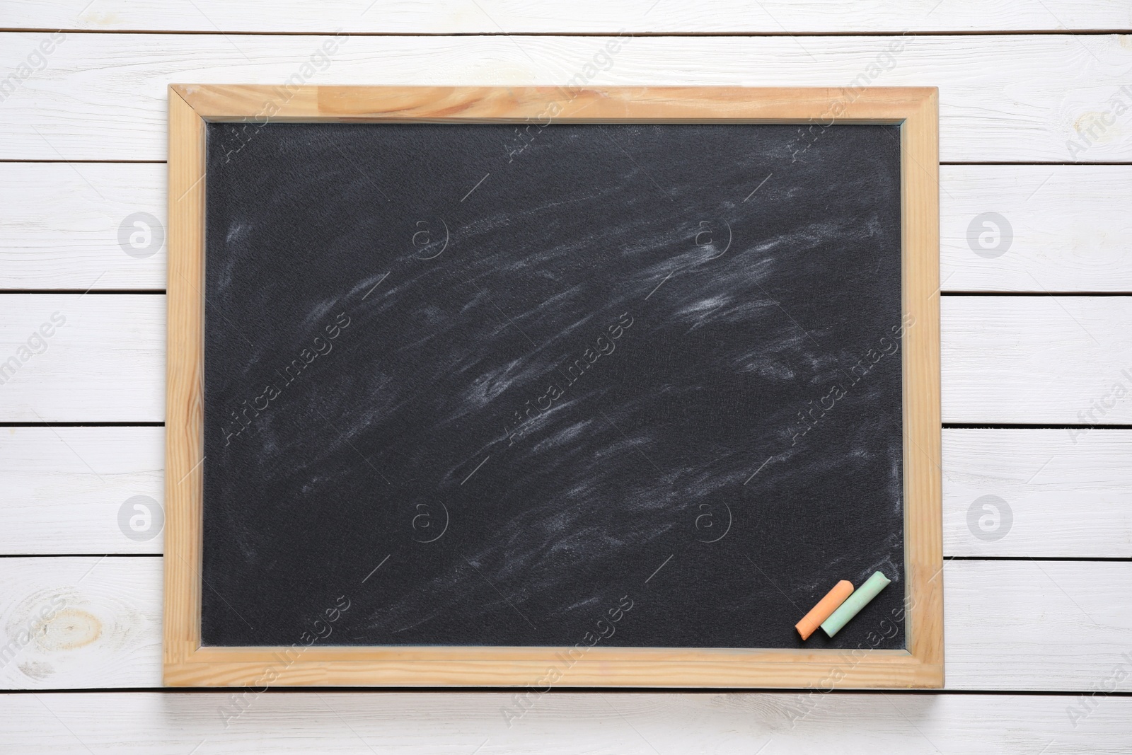 Photo of Blackboard with pieces of color chalk on white wooden background, top view. Space for text