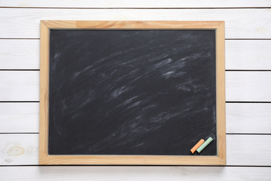 Photo of Blackboard with pieces of color chalk on white wooden background, top view. Space for text