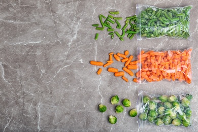 Plastic bags with different frozen vegetables on table, top view