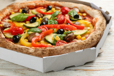 Photo of Delicious vegetable pizza in cardboard box on white wooden table, closeup