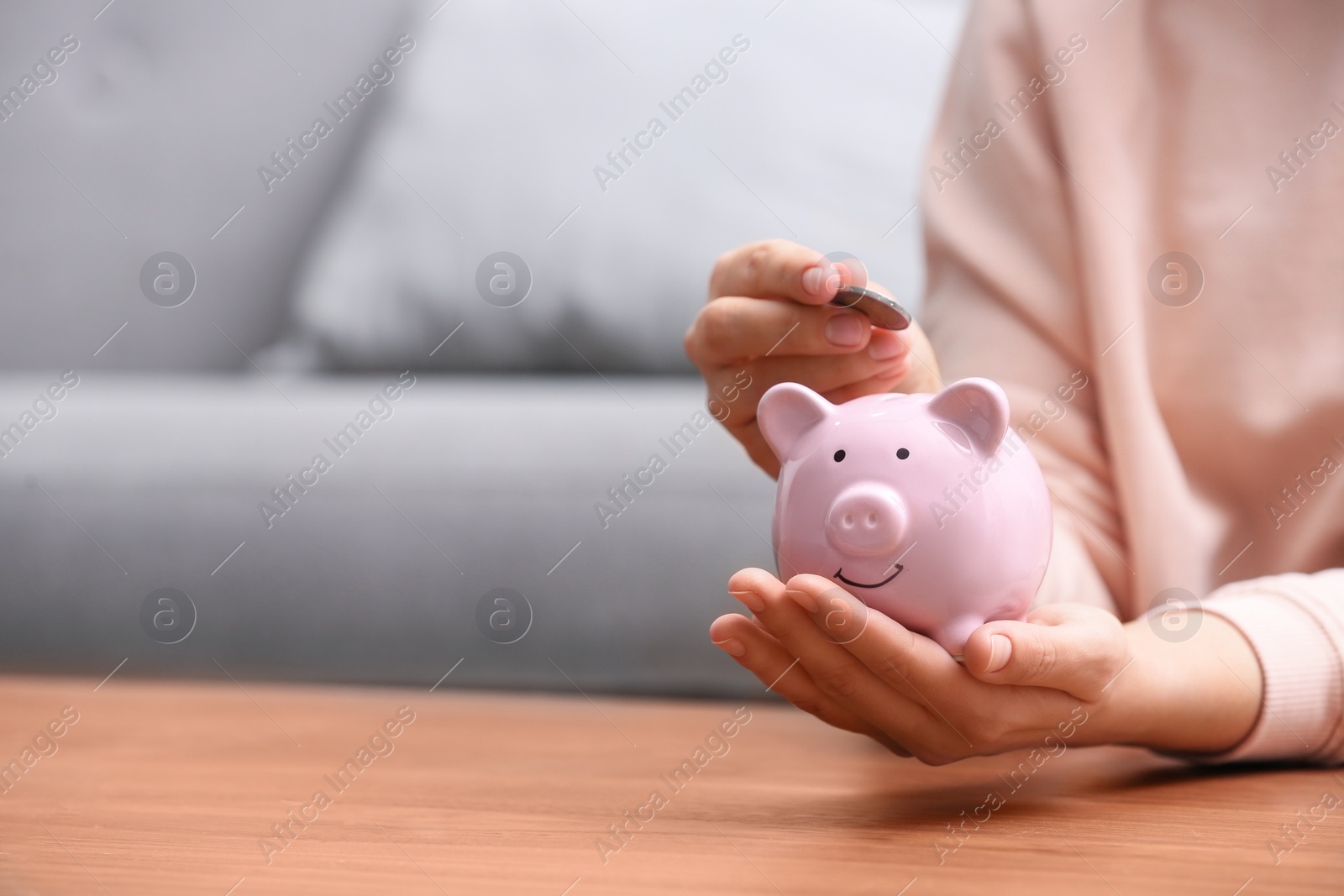 Photo of Woman putting coin into piggy bank at wooden table, closeup. Space for text