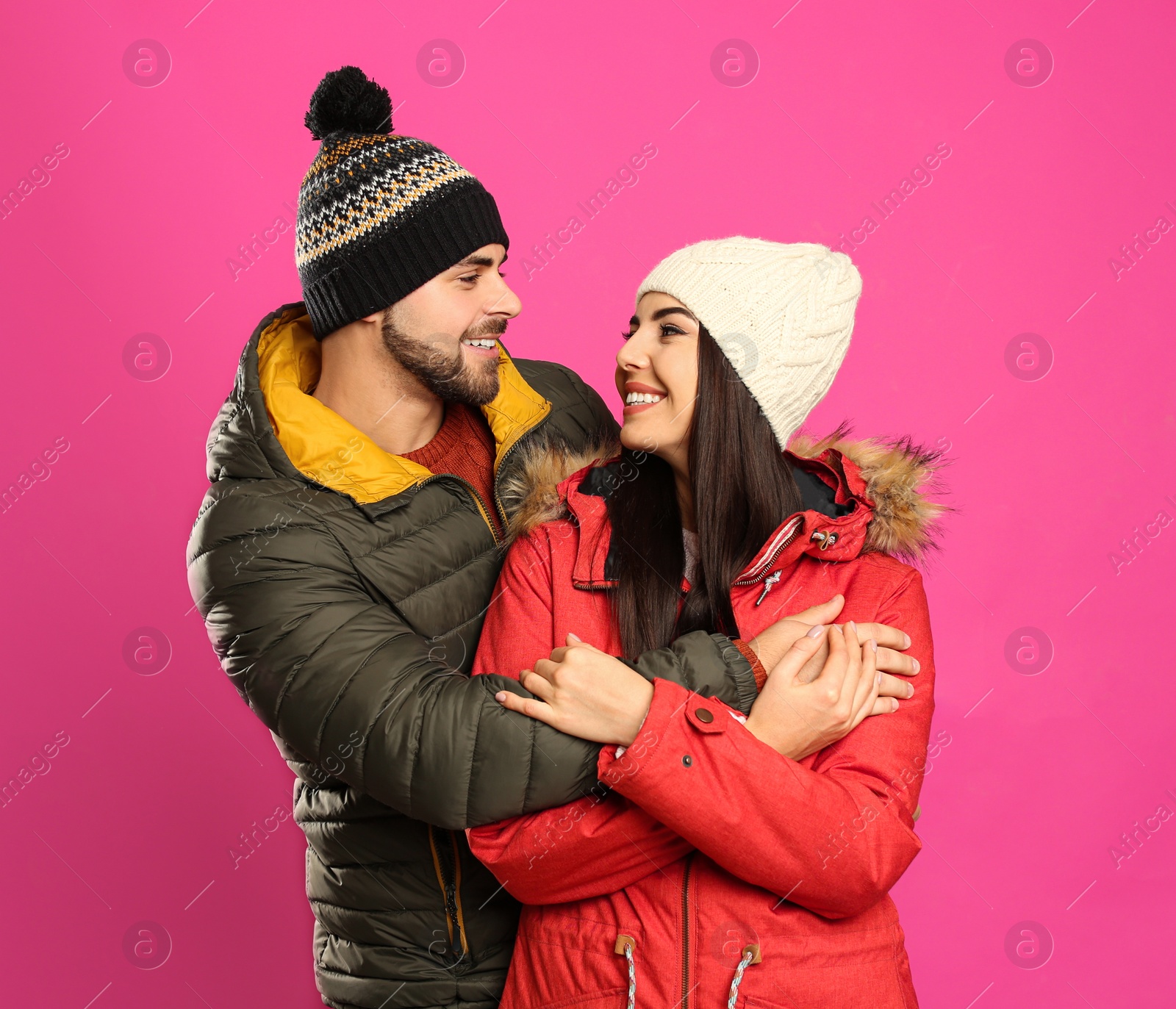 Photo of Happy young couple in warm clothes on pink background. Winter vacation